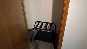 Ein schmales Zimmer mit Holztür, einem kleinen Metallregal und einem Kleiderständer mit gefalteter Kleidung.