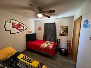 A bedroom with a bed, a ceiling fan, a door, and sports-themed decorations. - Relax Enjoy Mid-Missouri with Fenced in Back Yard (Boonville)