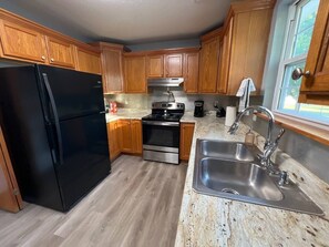 A kitchen with wooden cabinets, a black refrigerator, stainless steel appliances, and a granite countertop. - Relax Enjoy Mid-Missouri with Fenced in Back Yard (Boonville)