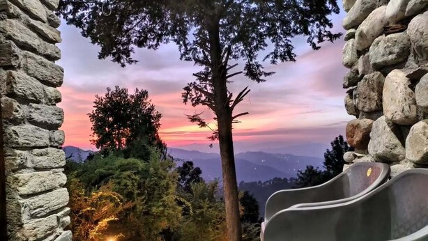 A stone wall, a wooden table with a glass, and a metal slide. - Mandeva Wooden castle (Bhikyasain)