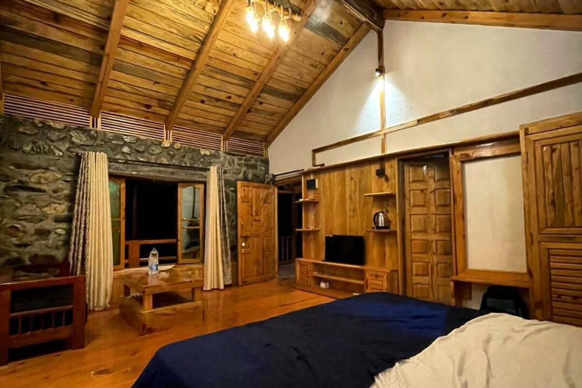 Une pièce rustique en bois, avec un lit, un mur en pierre, des étagères en bois et un téléviseur.