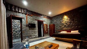 A cozy room with stone walls, a bed, a wooden table with a bottle and keys, and a bench. - Mandeva Wooden castle (Bhikyasain)