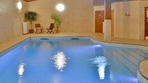 Une piscine intérieure avec des murs carrelés, un plancher en bois et deux plantes en pot.
