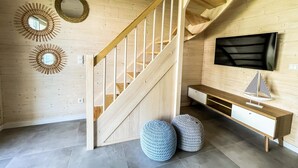 A wooden interior with a staircase, a TV mounted on the wall, and two round ottomans on the floor. - Cottage Near Kopan Beach and Lake (Darlowo)