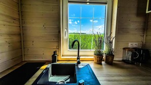 A modern kitchen with a black countertop, a sink, and a window with a view of a green field and wind turbines. - Cottage Near Kopan Beach and Lake (Darlowo)