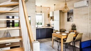 A modern kitchen with wooden cabinets, a dining table with chairs, and a staircase. - Cottage Near Kopan Beach and Lake (Darlowo)