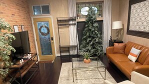 Una sala de estar con pared de ladrillo, un árbol de Navidad, un sofá, una mesa de centro y una televisión.