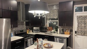 Una cocina moderna con armarios oscuros, un refrigerador de acero inoxidable, un horno empotrado y una isla grande con una cafetera y un portavasos para tazas.