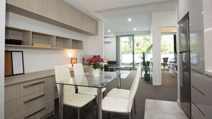 A modern kitchen with a glass dining table, white chairs, and built-in cabinets. - Kozyguru | Epping | Stylish 1 Bedroom Apartment (Epping)