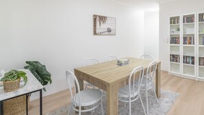 A dining area with a wooden table and white chairs, a bookshelf with books, and a framed picture on the wall. - Kozyguru | Homebush West | 3-Beds Apt With Parking (Homebush West)