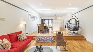 A spacious living area with a red sofa, a dining table, and a hanging chair. - Kozyguru | Rose Bay | Charming House Near Beach (Rose Bay)