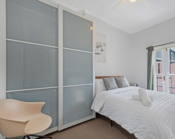 A bedroom with a bed, a chair, a sliding glass door, and a window with curtains. - Kozyguru | Surry Hills | Classic Terraced House (Surry Hills)