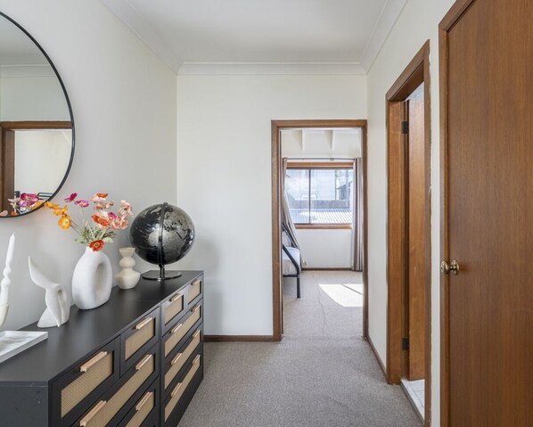 A hallway with a dresser, a mirror, and a globe. There is a door on the right and a window at the end of the hallway. - Kozyguru | Balmain | Townhouse bridge view or Charming Comfy Studio (Balmain)