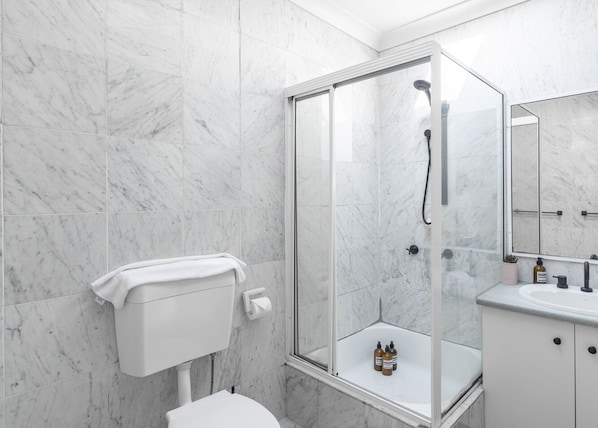 A modern bathroom with a glass-enclosed shower, a toilet, and a sink with toiletries. - Kozyguru | Balmain | Townhouse bridge view or Charming Comfy Studio (Balmain)