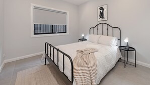 Un dormitorio con cama, mesitas de noche, una ventana y una obra de arte colgada en la pared.