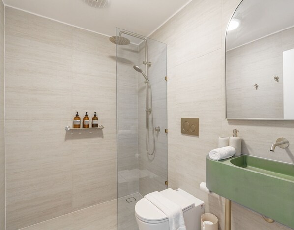 A modern bathroom with a glass shower enclosure, a green sink, and a white toilet. - Kozyguru | Forestville (Forestville)