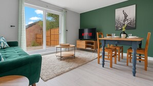 Un salon moderne avec un canapé vert, une table à manger avec des chaises, un téléviseur et un tableau accroché au mur.