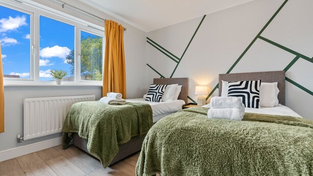 Une chambre d’hôtel avec deux lits, une fenêtre donnant sur des arbres, un radiateur et une lampe sur une table de chevet.