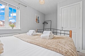 Ett sovrum med en säng, två hoprullade handdukar, ett fönster med utsikt, en tavla och en dörr.