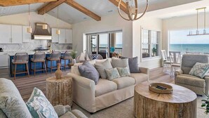A spacious living area with a large sofa, a round coffee table, and a view of the ocean through large windows. - Beachfront Luxury Villa in Dewey Beach, Two Master Bedroom (Dewey Beach)