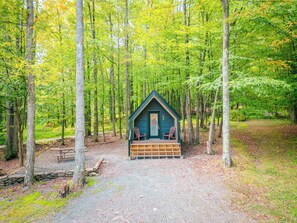 A cabin in a forest with a porch and two chairs. - A-frame Principal (Wellsboro)