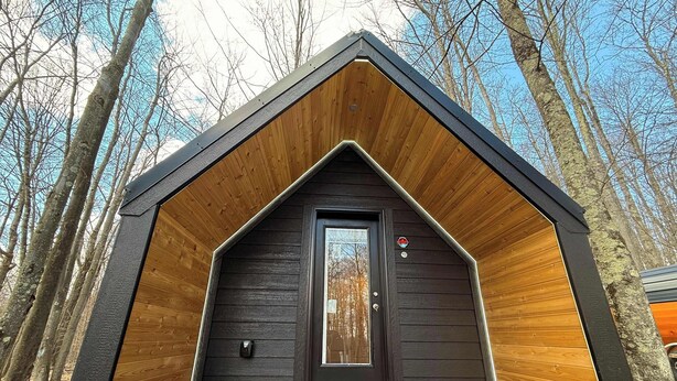 Une cabane à l’extérieur sombre, avec une porte d’entrée en bois et un petit porche.