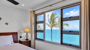 A hotel room with a large window offering a view of the sea and palm trees. - Watch Whales from your Bed - Double Master Sunset Suite (Kihei)