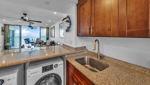 A modern kitchen with granite countertops, wooden cabinets, and a built-in washing machine. - Watch Whales from your Bed - Double Master Sunset Suite (Kihei)