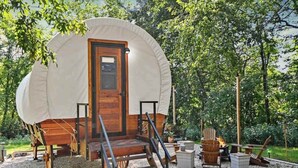 A covered wooden structure with a door, surrounded by outdoor seating and a fire pit. - Conestoga Wagon (Wellsboro)