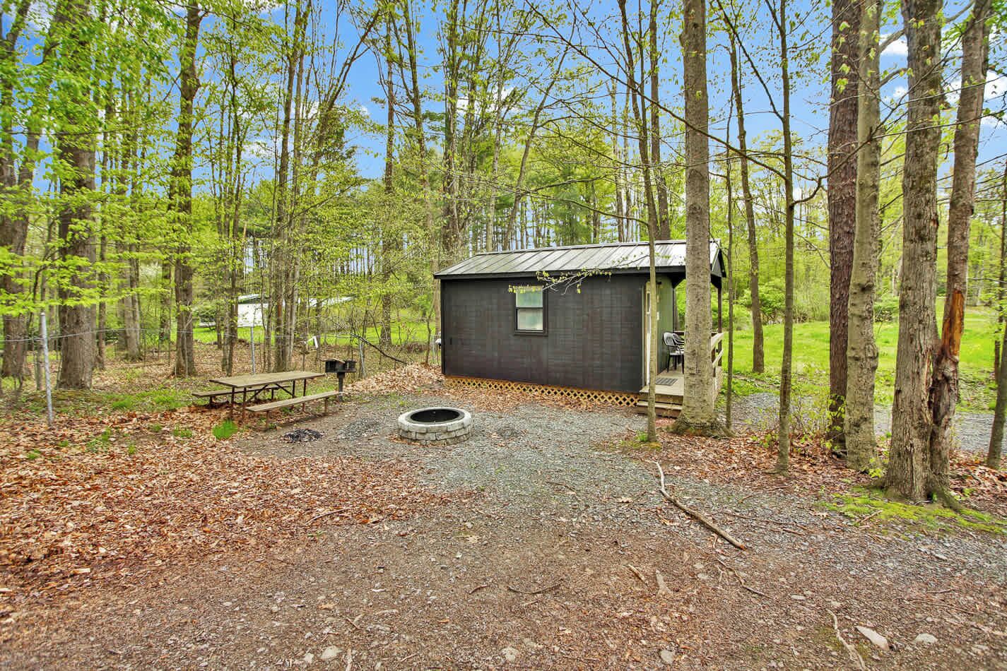 A rustic cabin with a gravel ground, a picnic table, and a fire pit.