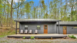 A cabin with a porch, four Adirondack chairs, and a door. - Cabin full bath (Wellsboro)