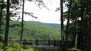 A forested area with a wooden fence and a bench. - Pop up Camper Site Water & Electric Up to 32FT (Wellsboro)