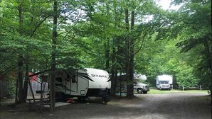 A campsite with a white RV and a truck parked on a gravel path surrounded by trees. - Pop up Camper Site Water & Electric Up to 32FT (Wellsboro)