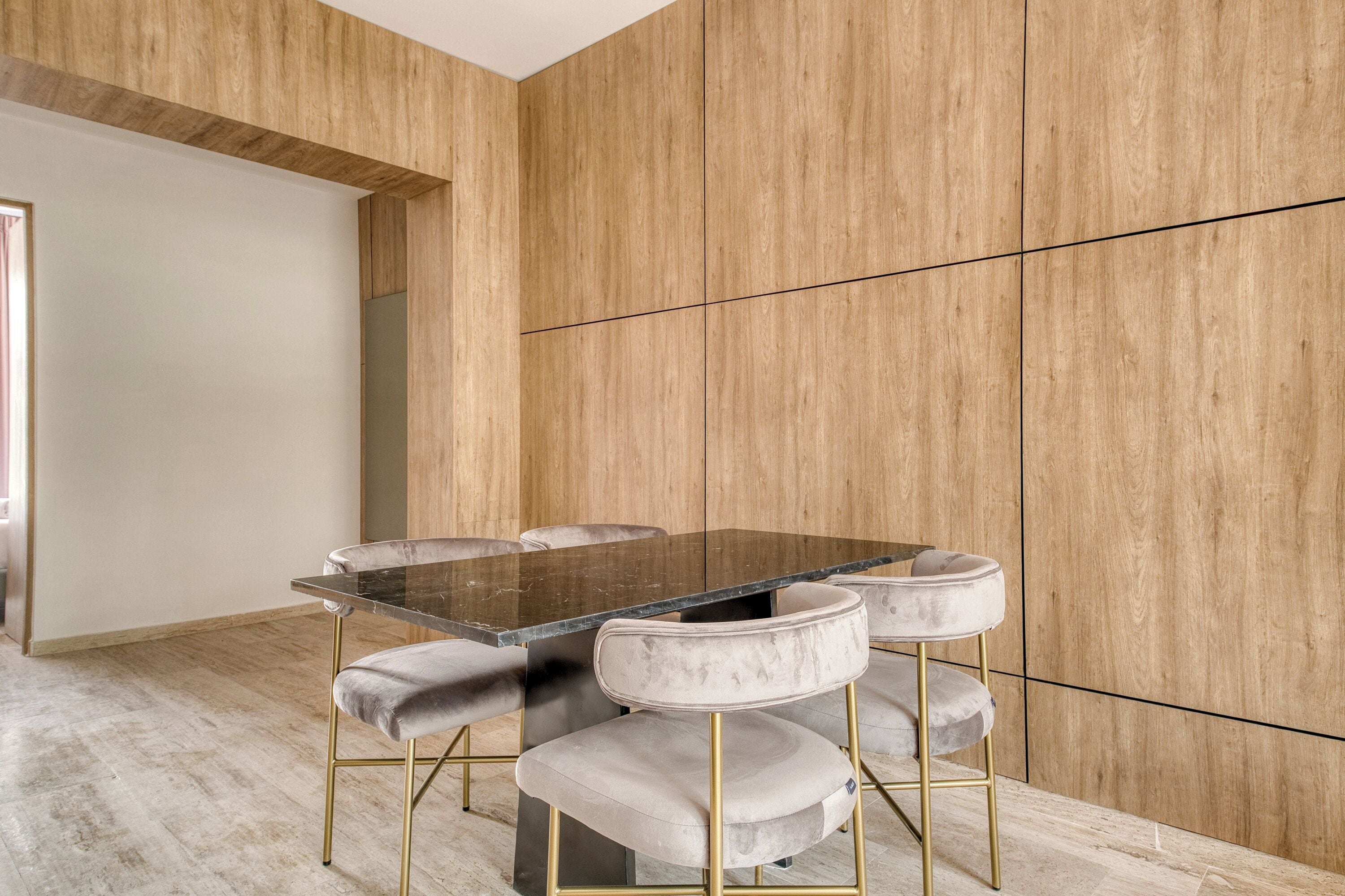 Un espace repas moderne, avec une table en marbre et des chaises rembourrées, le tout mis en valeur par un mur en bois orné d’un motif géométrique.
