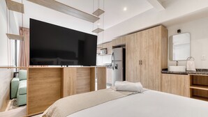 A modern hotel room with a large bed, a flat-screen TV, wooden cabinetry, a built-in kitchen, and a bathroom with a mirror and sink. - Myla Chapultepec (Mexico City)