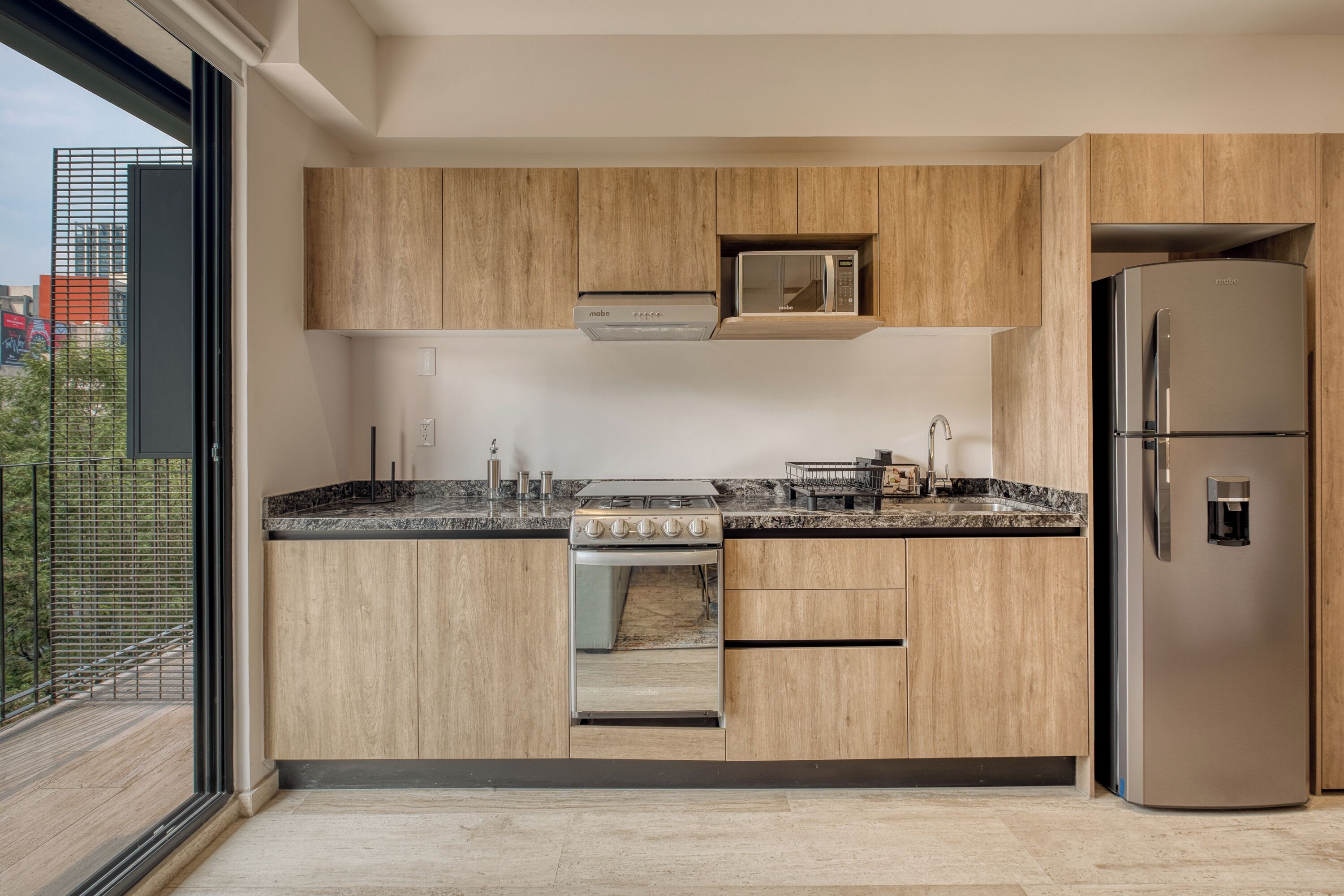 A modern kitchen with wooden cabinets, a stainless steel refrigerator, and a built-in oven.
