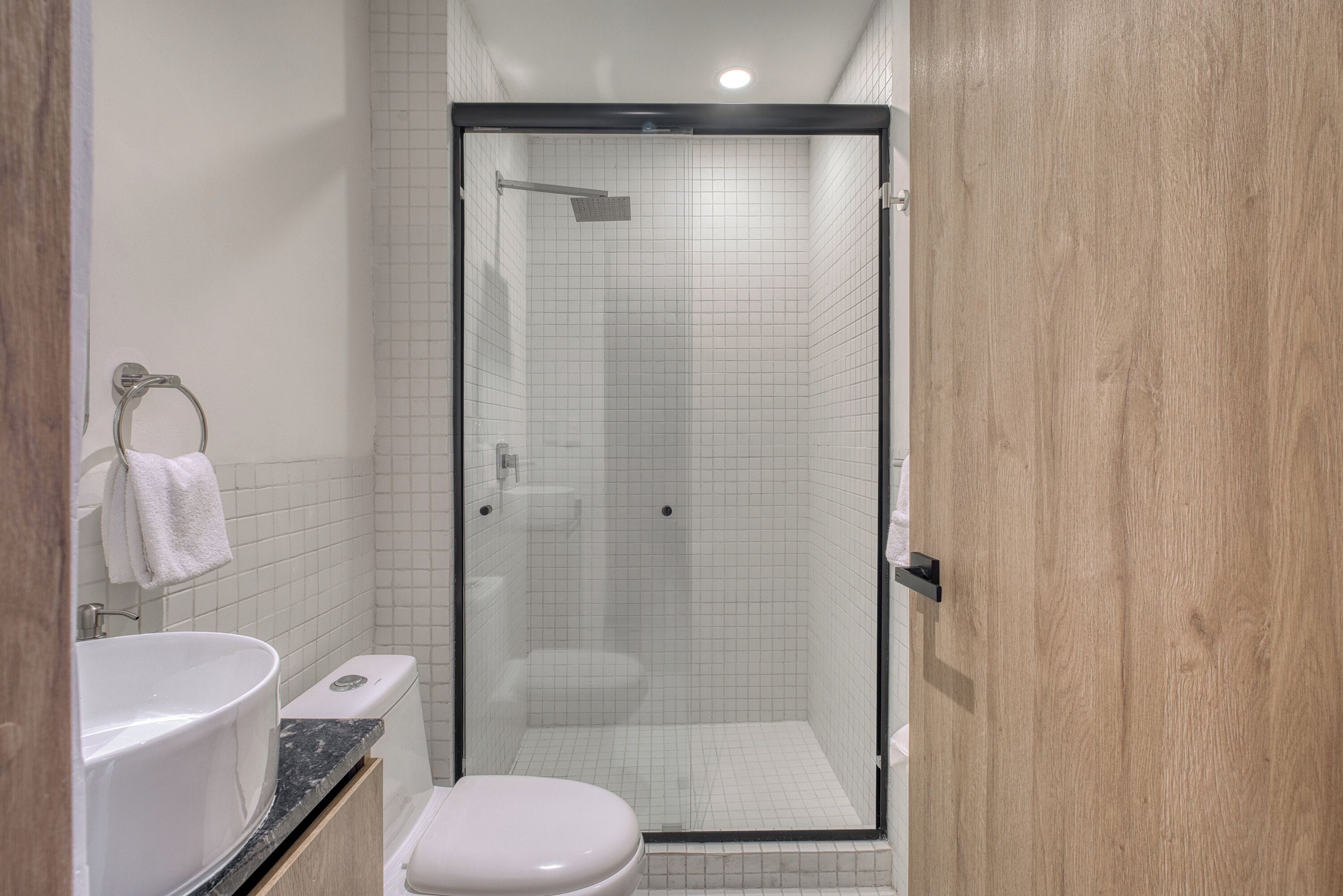 Un bany modern amb dutxa protegida per vidre, un vàter blanc i un lavabo amb taulell de marbre.