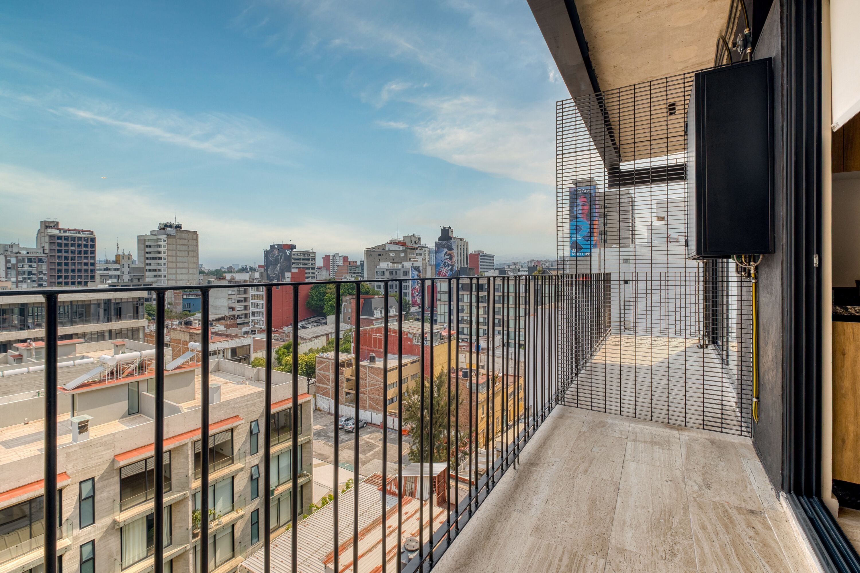 A balcony with a city view, metal railing, and a television mounted on the wall.