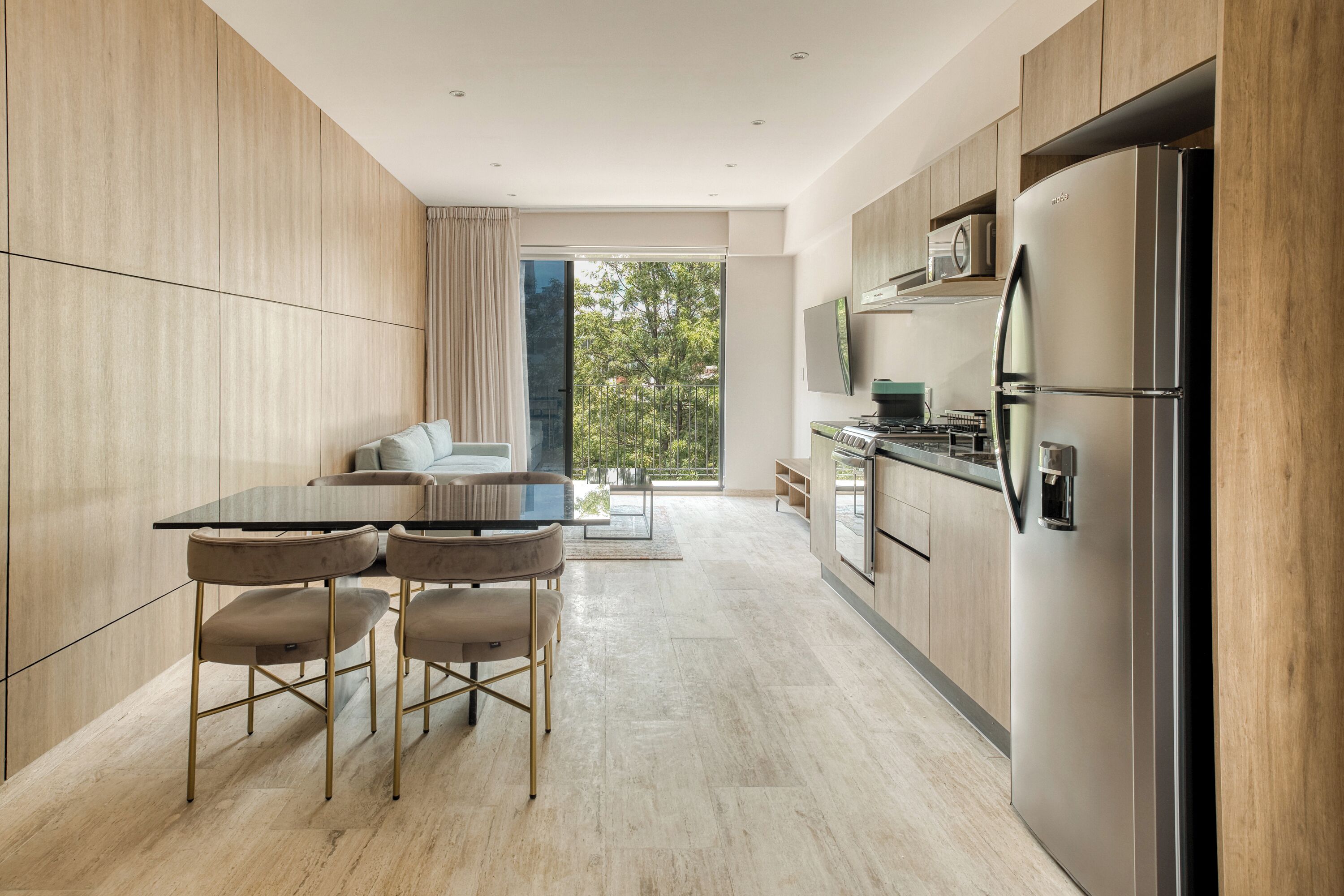 A modern kitchen with a dining area, large windows, and a view of greenery.
