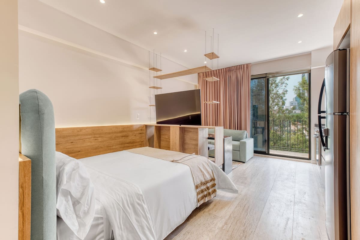 A modern hotel room with a large bed, a desk, a flat-screen TV, and a view of the outdoors.