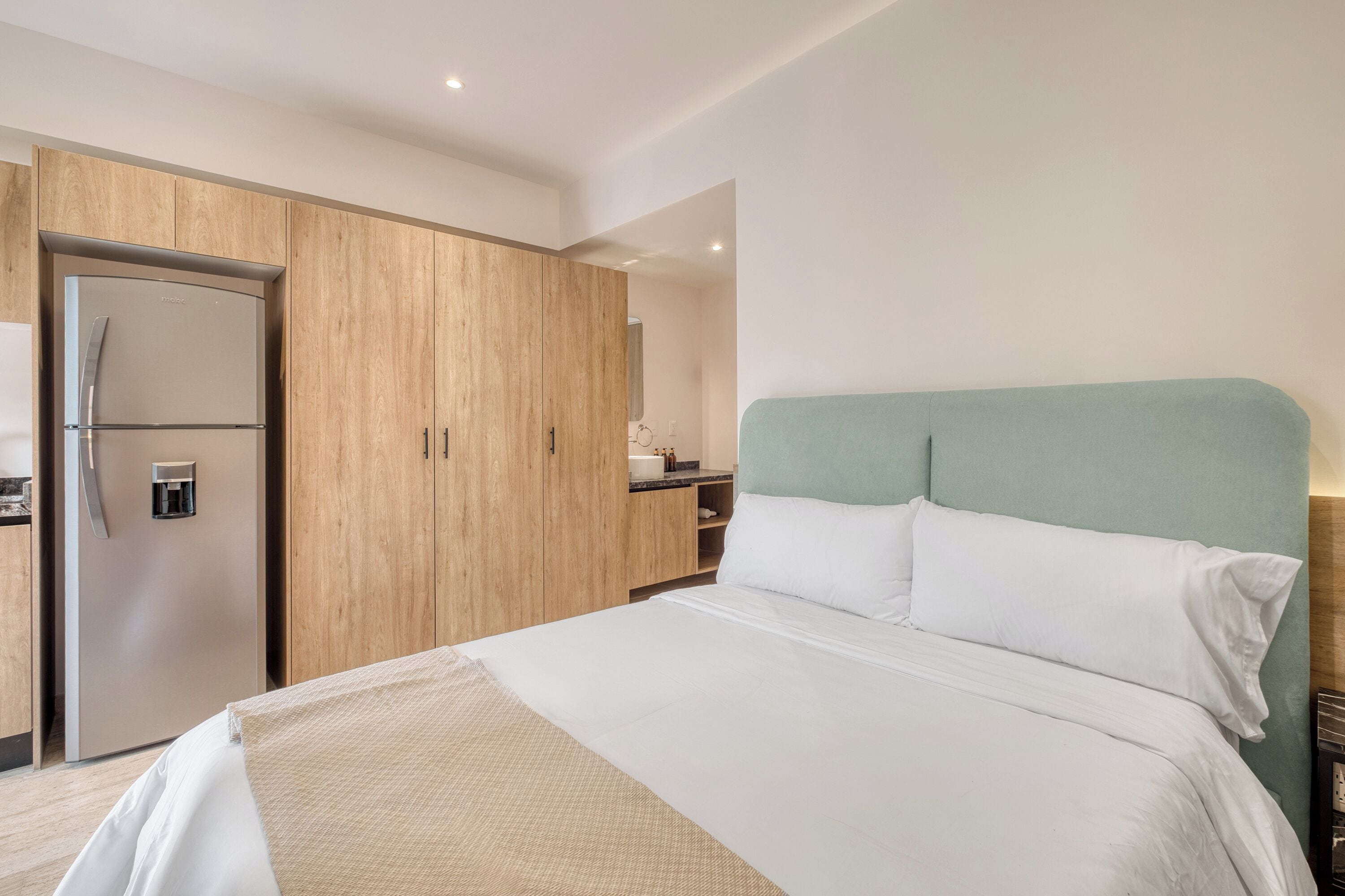 A hotel room with a bed, a wardrobe, a kitchenette, and a bathroom.