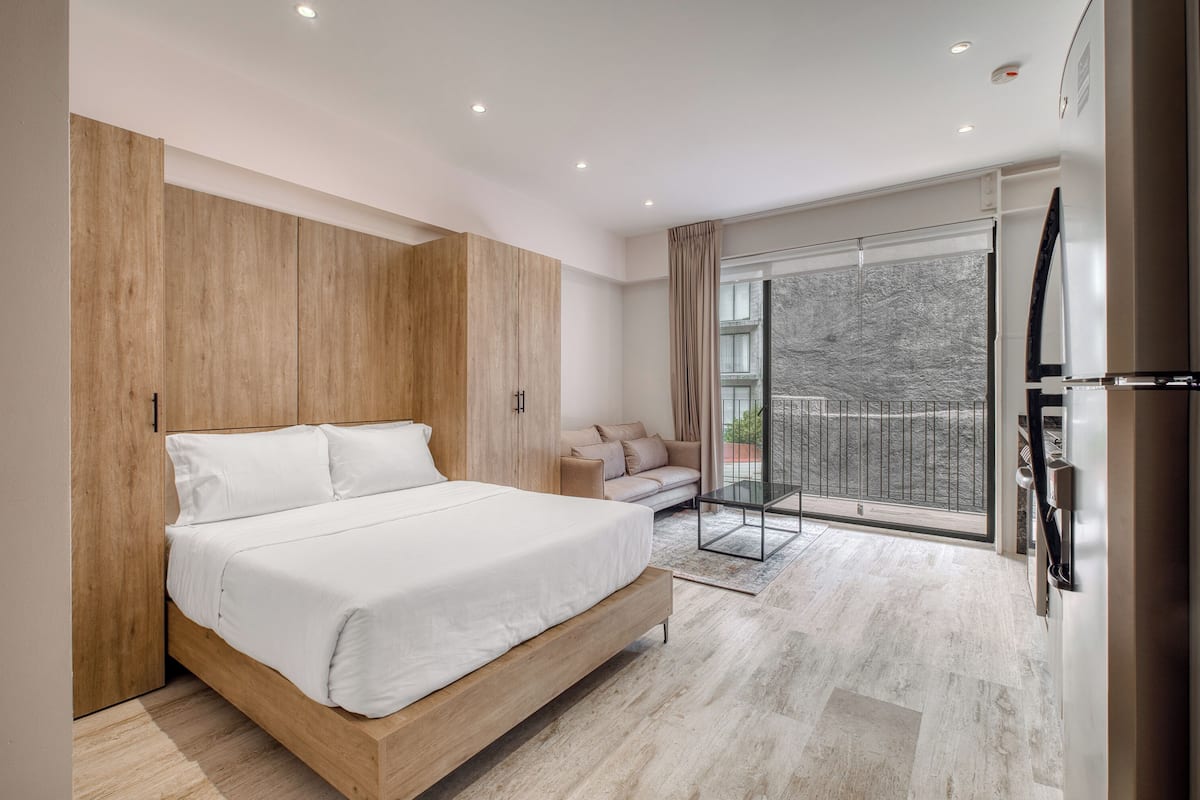 A modern bedroom with a large bed, a sofa, and a balcony with a view.