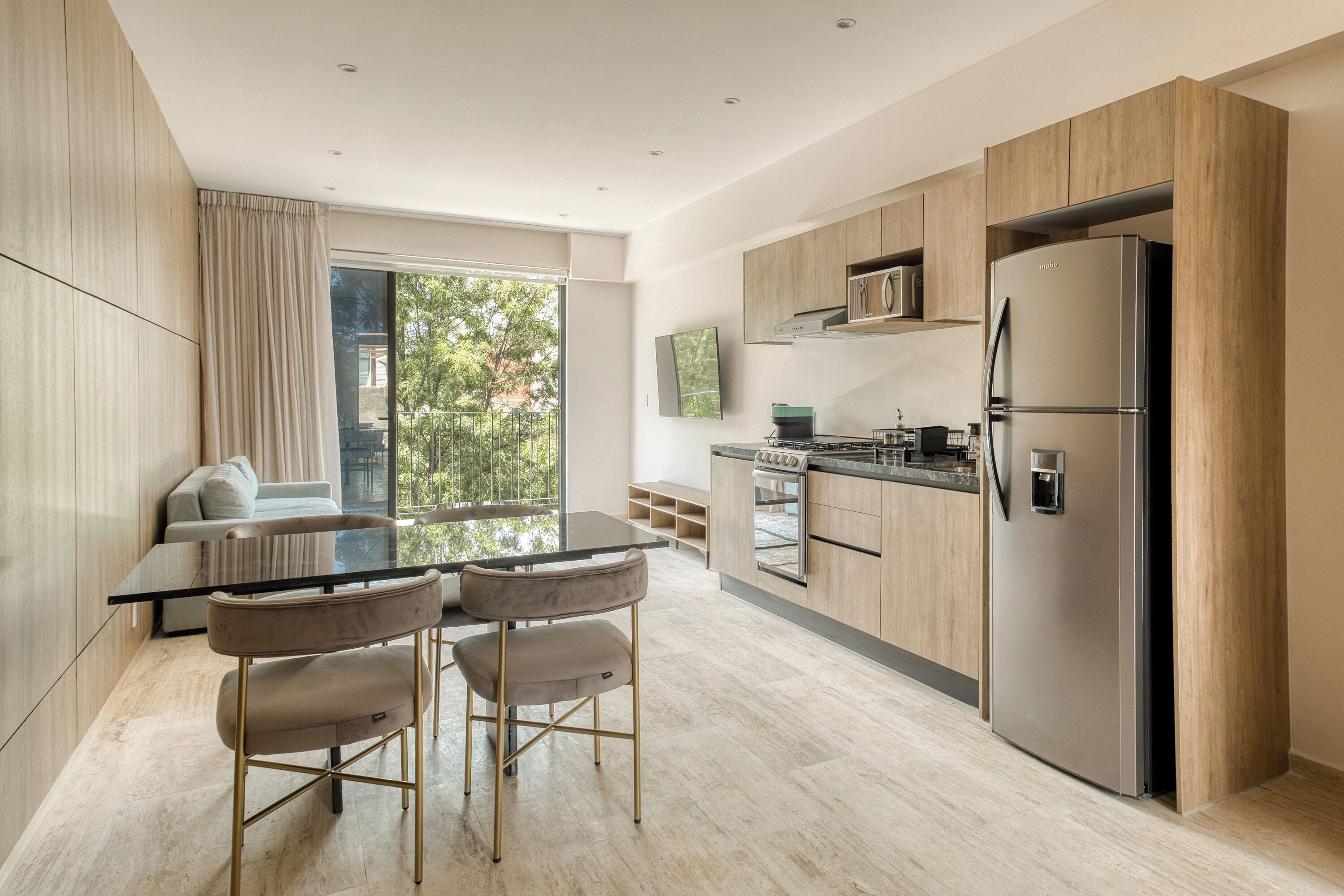 Eine moderne Küche mit einem großen Kühlschrank, Holzschränken und einem Essbereich mit einem Glastisch und Stühlen.
