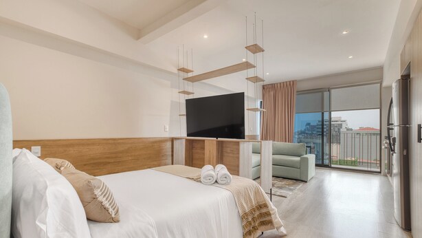 A modern hotel room with a large bed, a flat-screen TV, a balcony with a city view, and a kitchenette. - Myla Chapultepec (Mexico City)