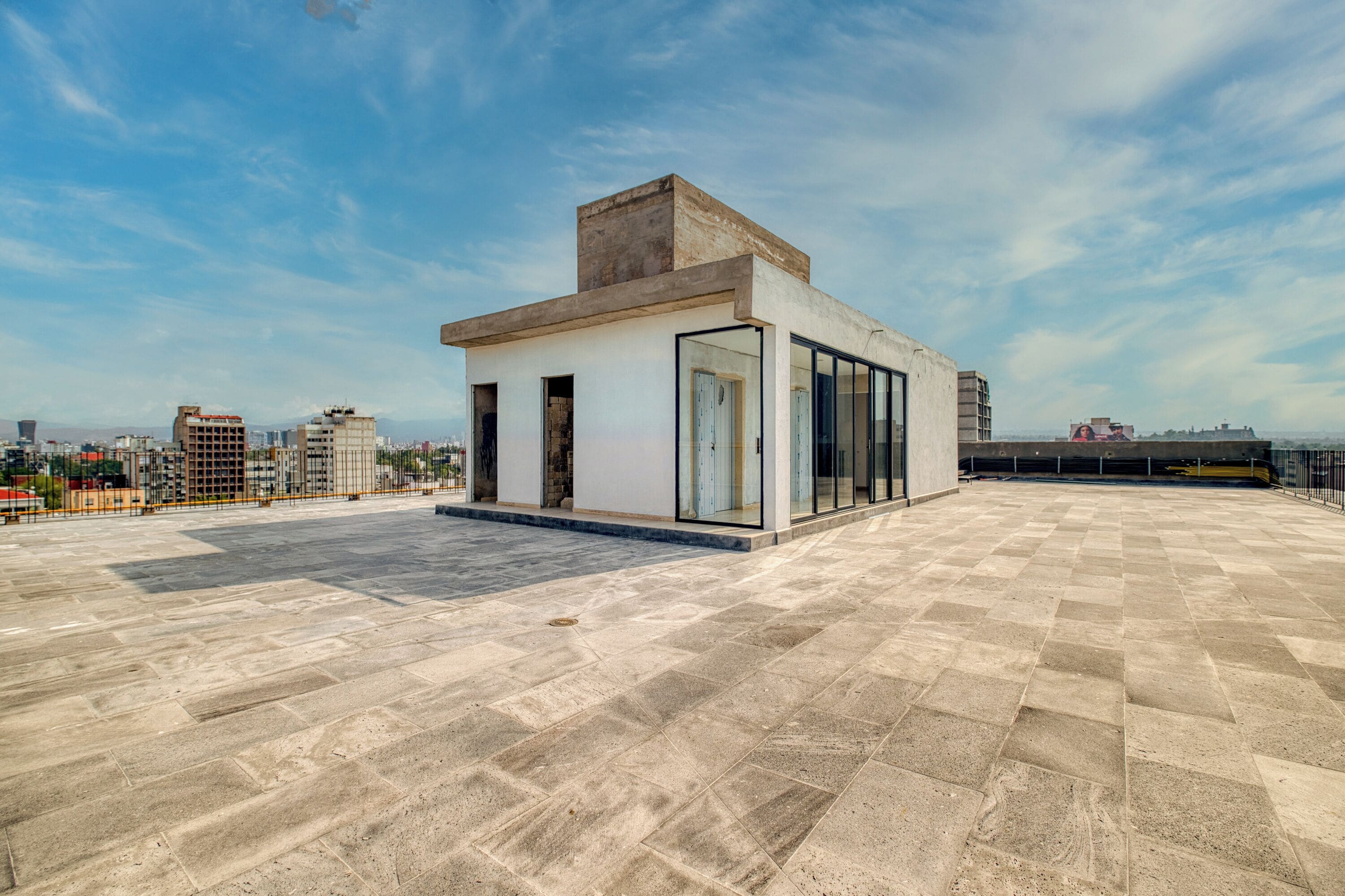 A rooftop terrace with a modern building, large windows, and a cityscape view.