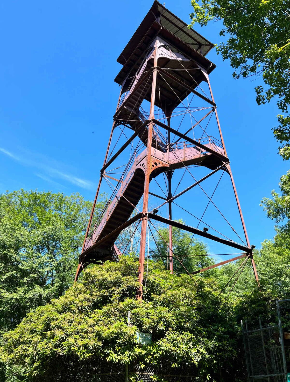Eine hohe, verrostete Metallkonstruktion mit Treppe, umgeben von dichtem Grün.