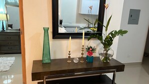 Ein Holzkonsolentisch mit einem Spiegel darüber, einer grünen Vase, einer Kerze und einer Pflanze mit einer roten Blüte.