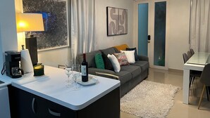 Ein modernes Wohnzimmer mit einem grauen Sofa, einer Kaffeemaschine, Weingläsern und einem Esstisch.