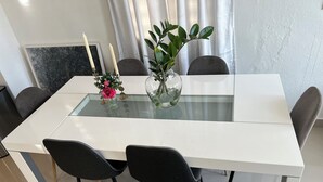 Ein moderner Esstisch mit Glasplatte, umringt von schwarzen Stühlen. Auf dem Tisch stehen zwei Vasen mit Blumen und Kerzen.