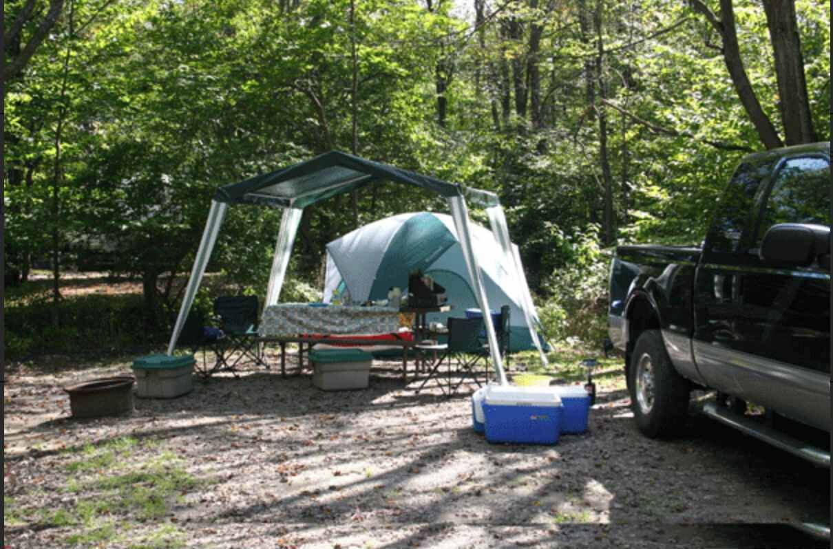 Un campamento con tienda de campaña, mesa, sillas y hielera.